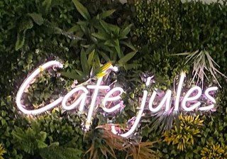 Enseigne lumineuse du Café Jules sur un mur végétal