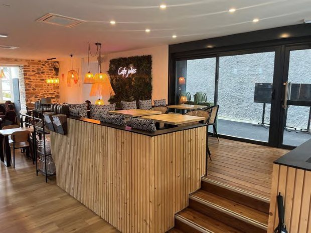 Salle du Café Jules, comptoir en bois et baies vitrées sur le gave, enseigne lumineuse sur mur végétal